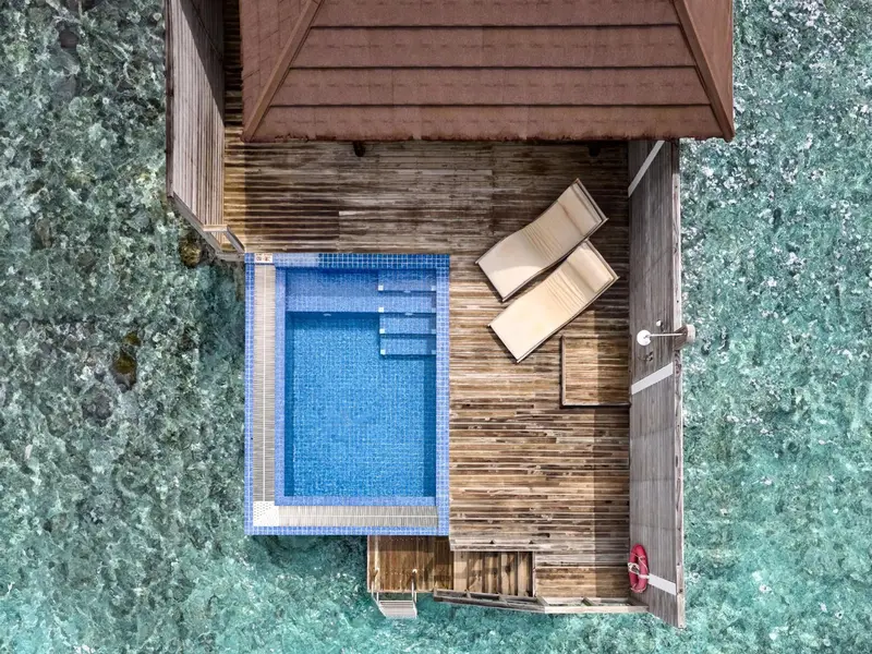 Vue aérienne d'une terrasse en bois avec une petite piscine et deux chaises longues.