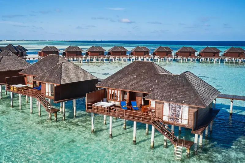 Vues aériennes de bungalows sur pilotis au-dessus d'une eau turquoise.