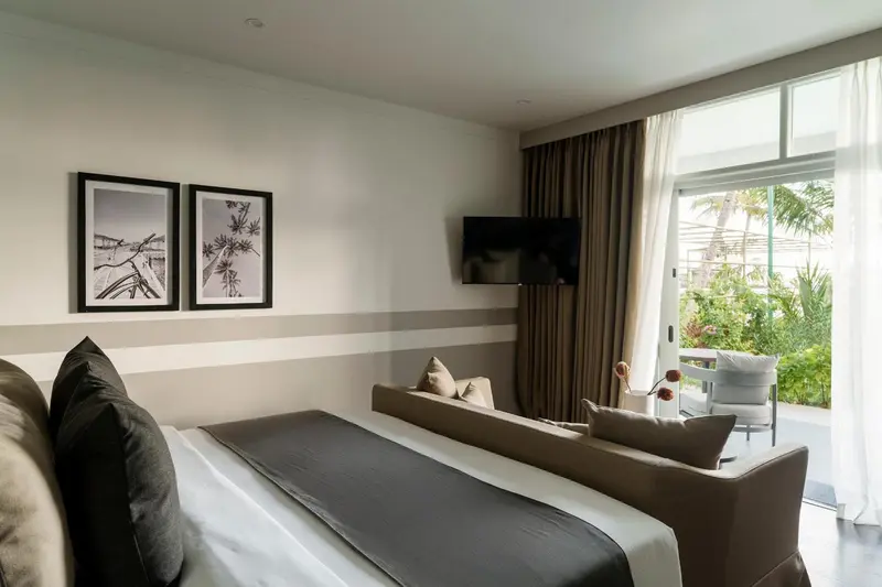 Une chambre avec un grand lit et un coin salon donnant sur une terrasse.
