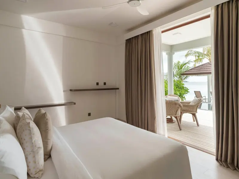 Une chambre lumineuse s'ouvre sur une terrasse avec vue sur la végétation et la mer.