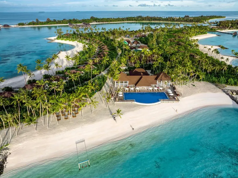Vue aérienne d'une île tropicale avec des bungalows et une plage de sable blanc.