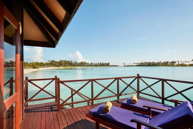 Terrasse en bois avec transats donnant sur une mer turquoise et une plage de sable blanc.
