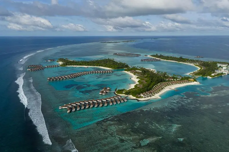 Vue aérienne d'un complexe hôtelier tropical entouré d'une eau turquoise et de plages de sable blanc.