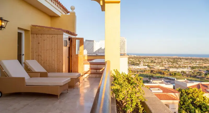 Deux chaises longues sur une terrasse ensoleillée avec vue sur la ville et la mer.