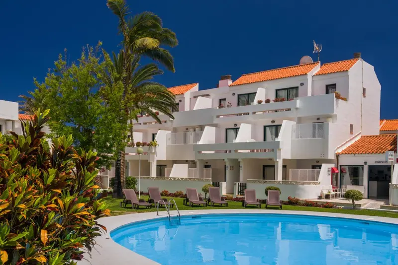 Bâtiment blanc à deux étages avec des balcons et une piscine au premier plan.