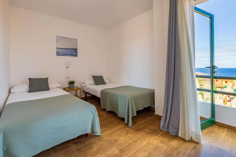 Une chambre lumineuse avec deux lits simples et un accès à un balcon.