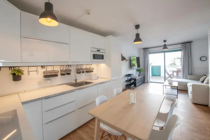 Une cuisine moderne et lumineuse s'ouvre sur un espace de vie avec canapé et table.