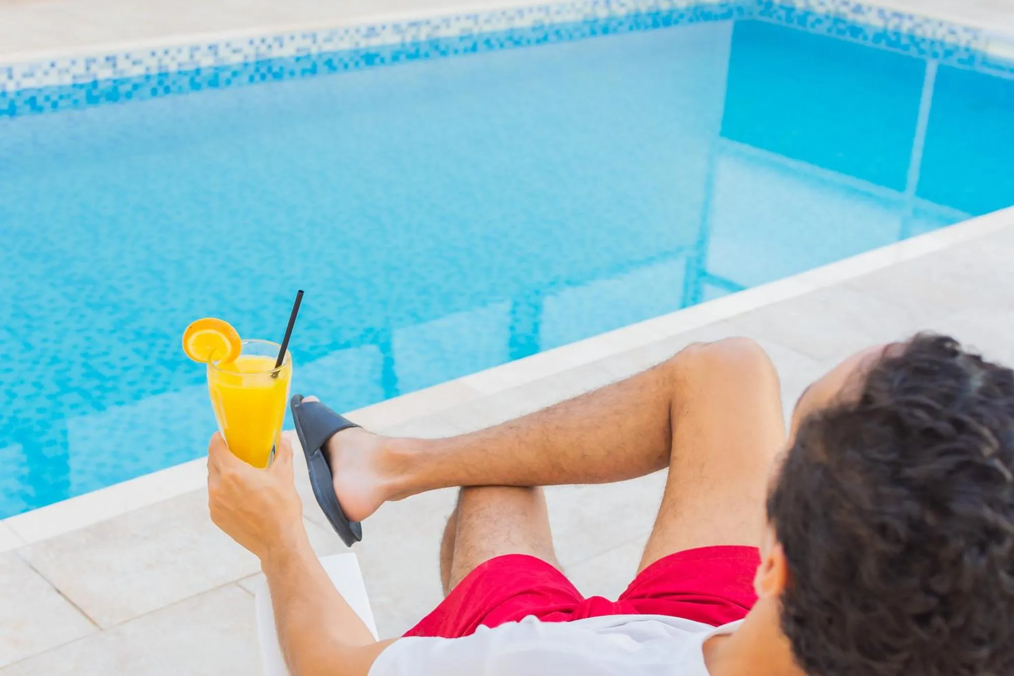 Une personne se relaxe au bord d'une piscine avec un cocktail.