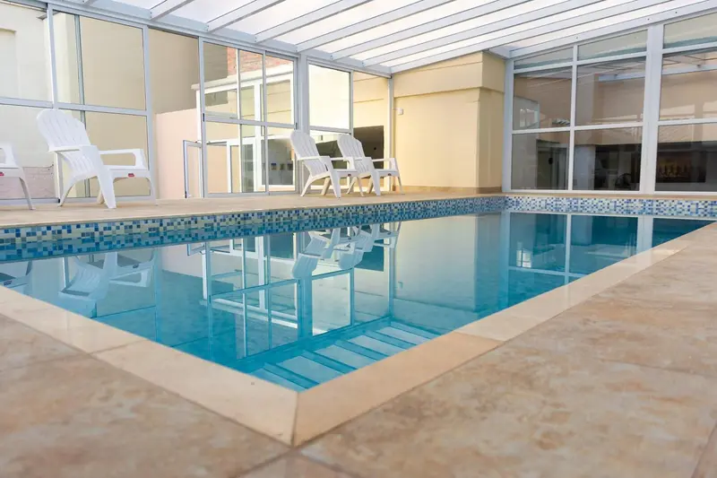 Une piscine interieure avec des transats blancs et un sol carrelé.