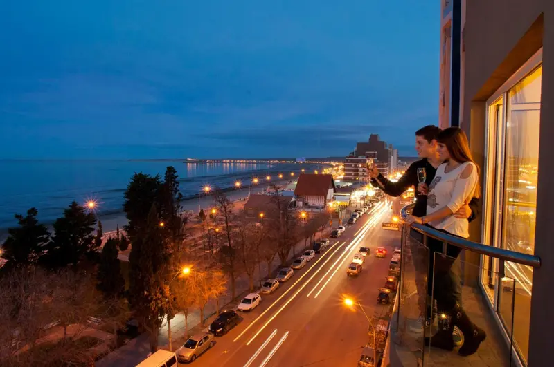 Un couple admire la vue nocturne sur la ville et la mer depuis un balcon.