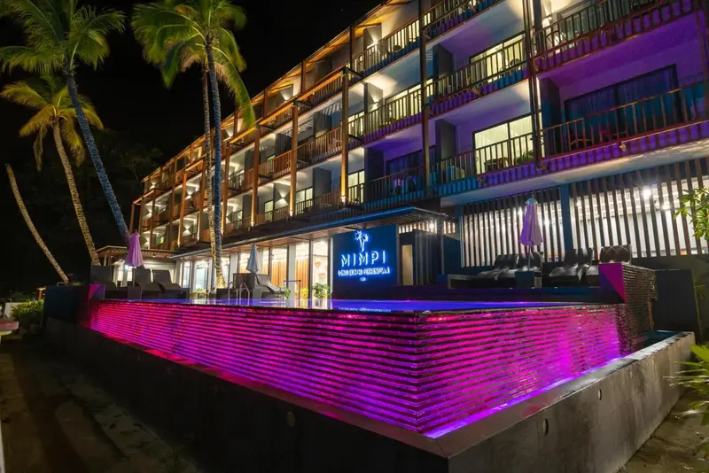 Façade d'un bâtiment illuminé avec une piscine au premier plan.