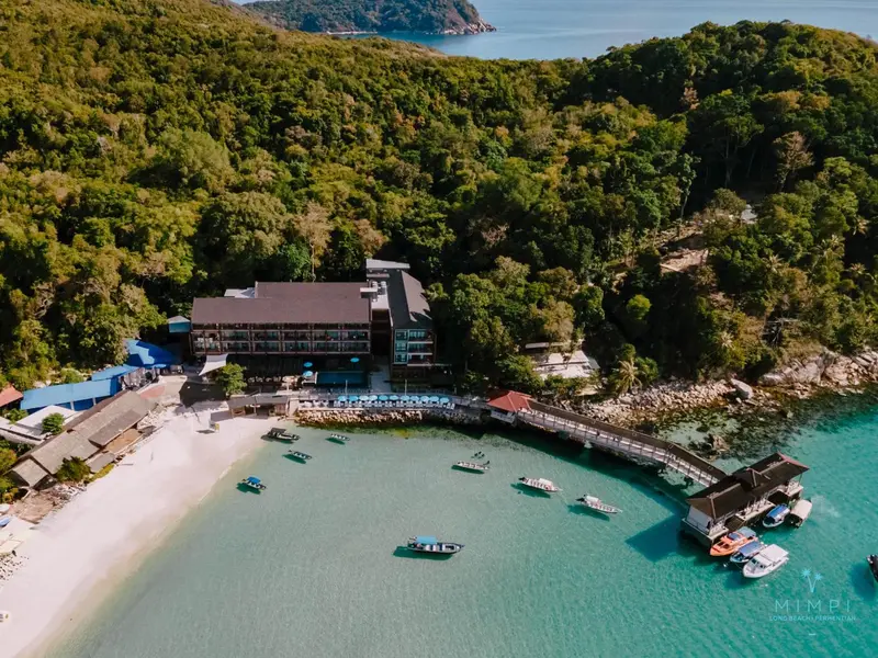 Vue aérienne d'une plage et d'un complexe hôtelier bordant une crique turquoise.