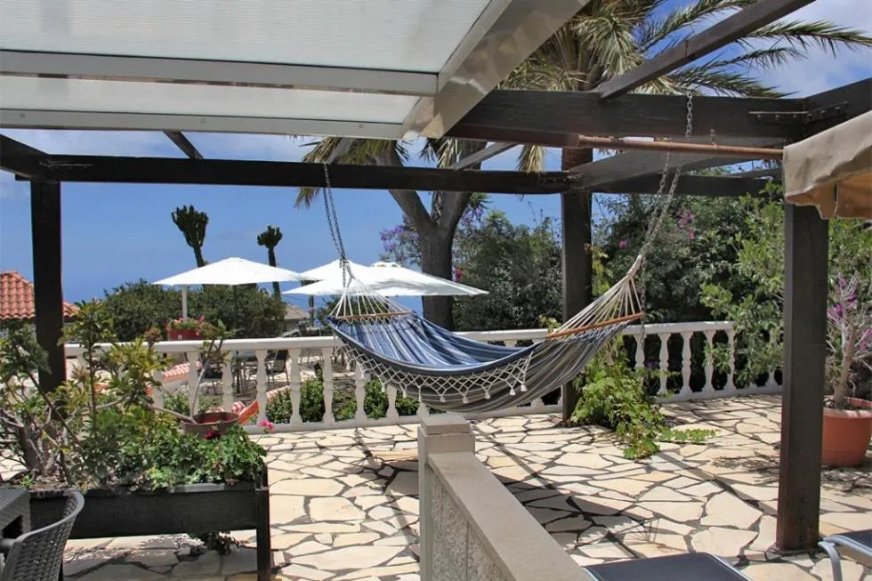 Un hamac bleu est suspendu sur une terrasse pavée avec vue sur la mer.