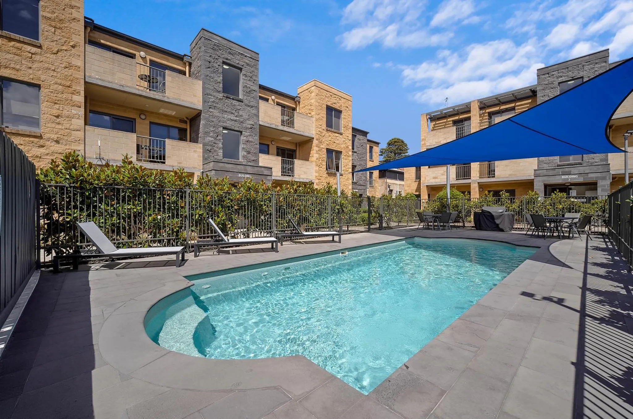Piscine rectangulaire entourée d'une terrasse avec des transats et un parasol bleu.