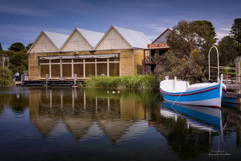 Bâtiment en bois clair au bord de l'eau avec un petit bateau amarré.