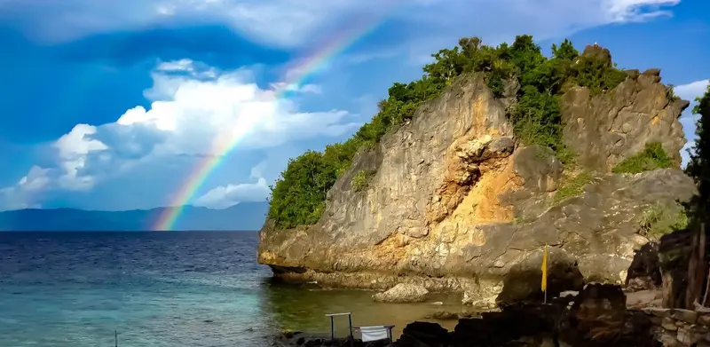 Un arc-en-ciel se dessine au-dessus d'une côte rocheuse et d'une mer calme.
