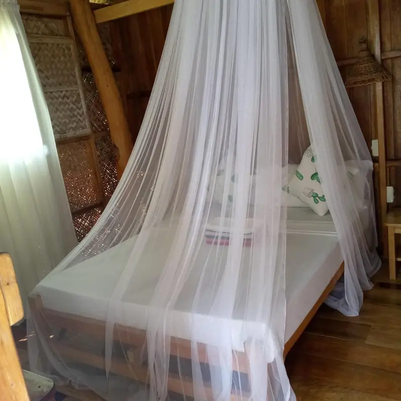 Lit recouvert d'une moustiquaire dans une chambre décorée de matériaux naturels.