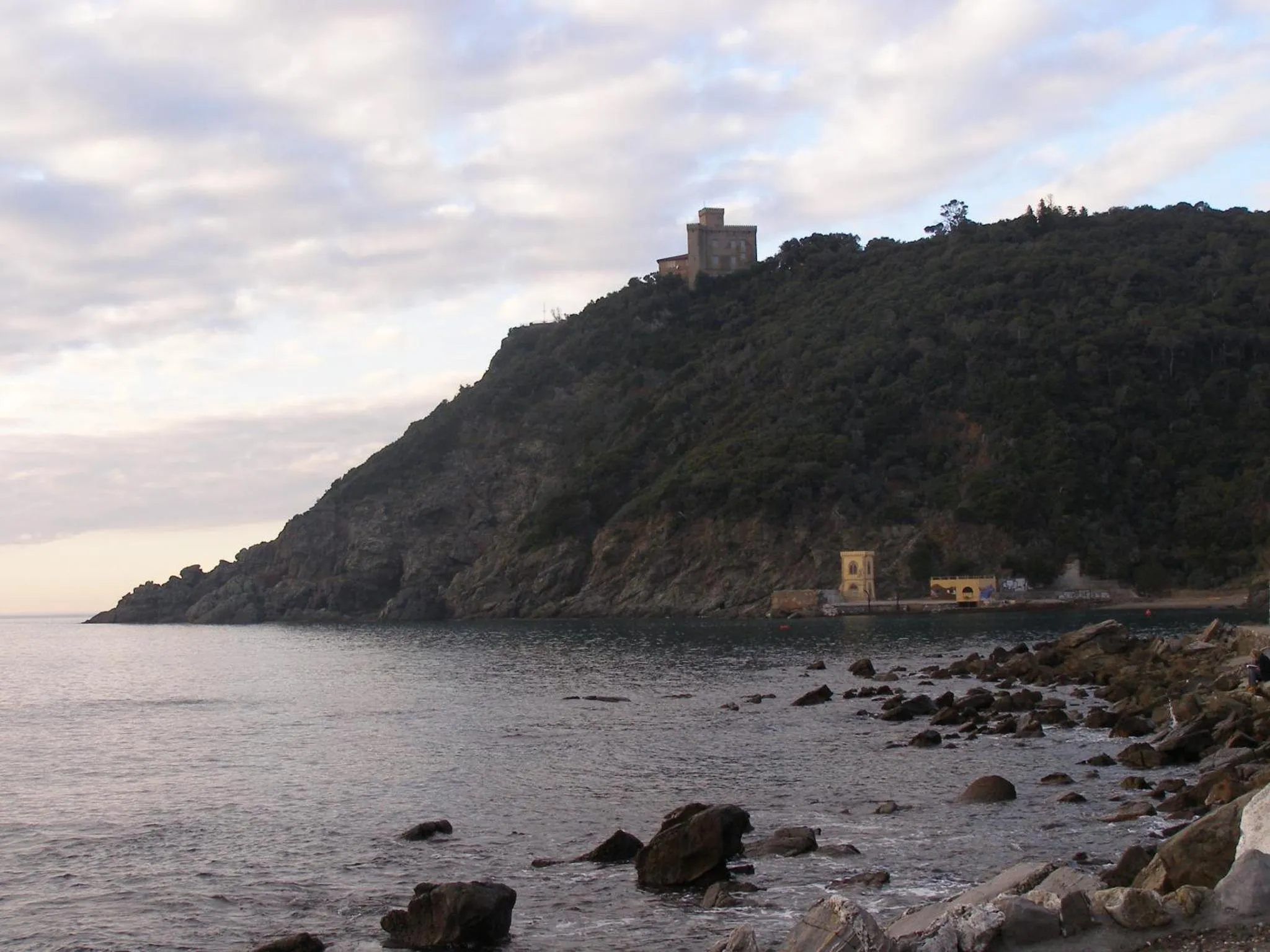 Côte rocheuse avec végétation et bâtiments au sommet d'une colline surplombant la mer.