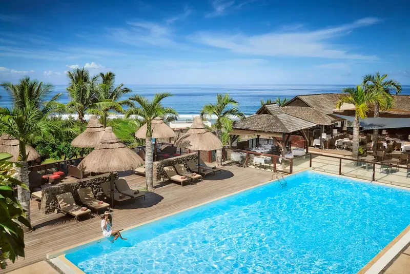 Une piscine turquoise bordée de transats et de parasols, avec vue sur la mer.
