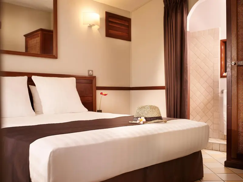 Une chambre lumineuse avec un grand lit recouvert de draps blancs et d'un couvre-lit marron.
