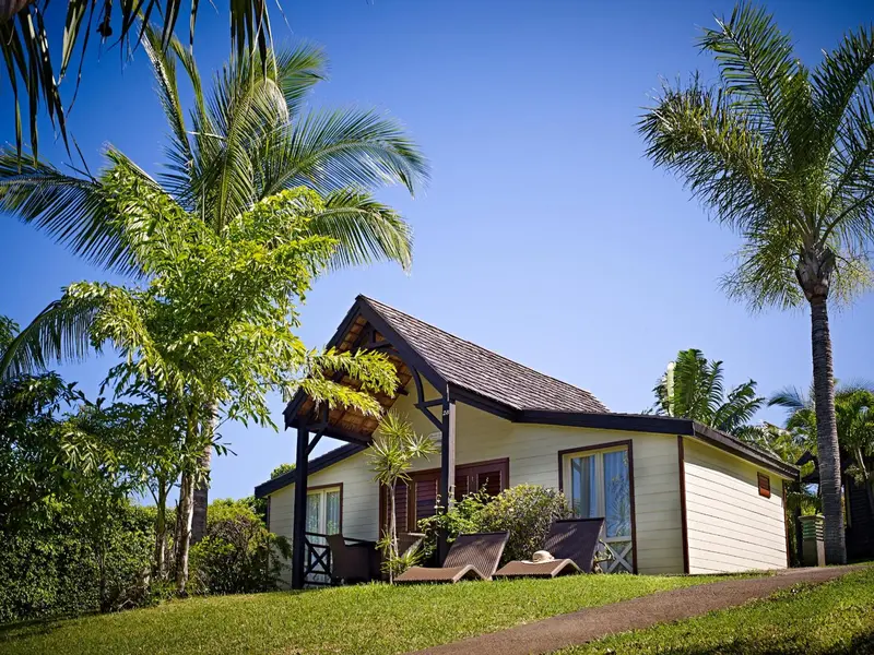 Maison de vacances avec toit en chaume et végétation tropicale.