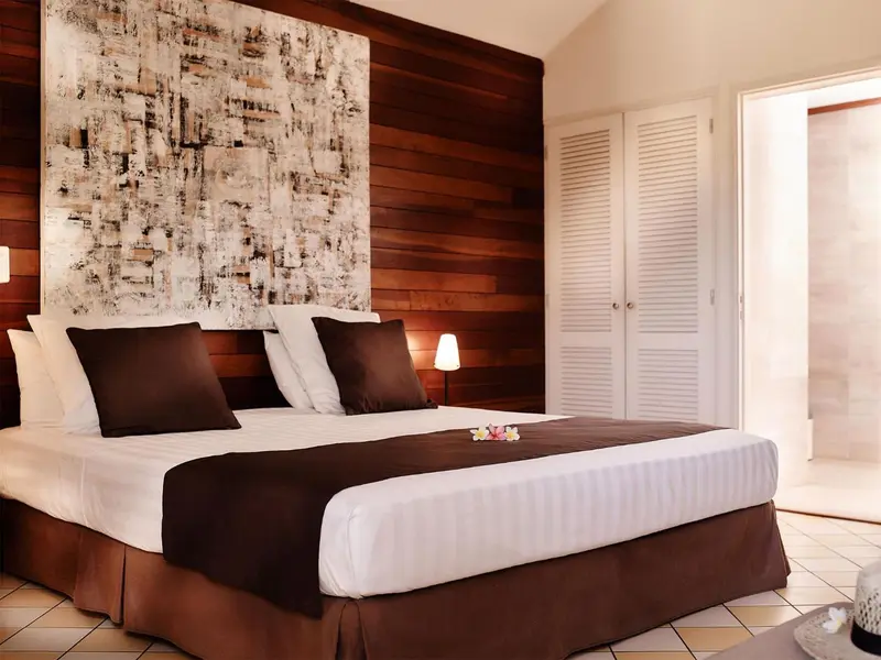Une chambre avec un grand lit recouvert d'une courtepointe blanche et de coussins foncés.