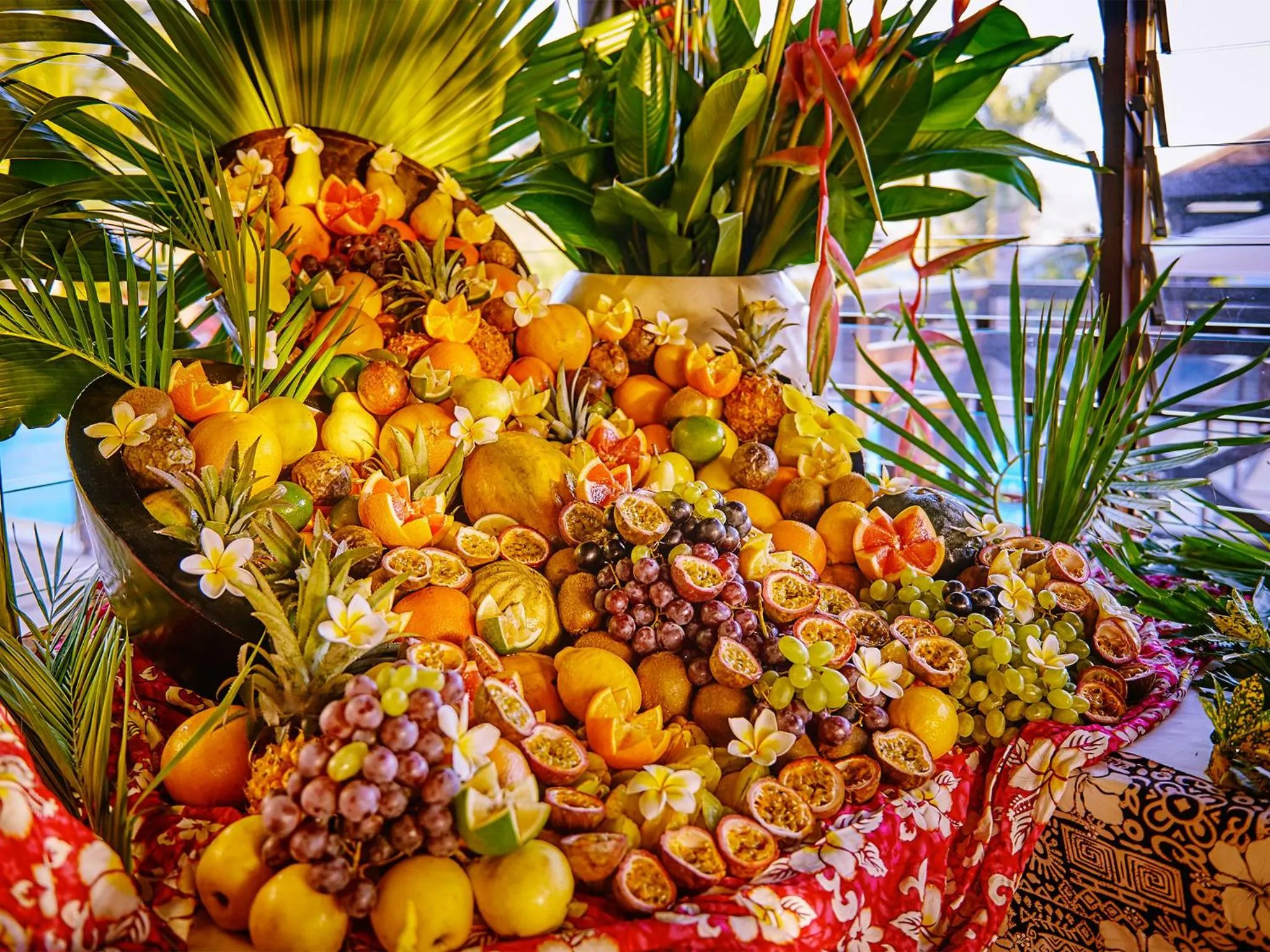Une abondante présentation de fruits frais et colorés, décorée de fleurs tropicales.