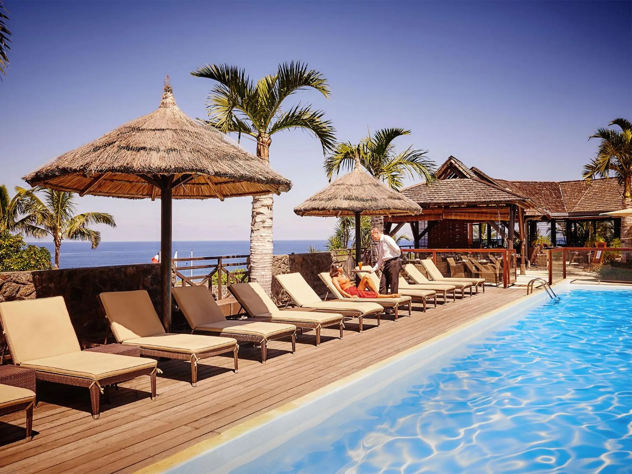Transats et parasols bordent une piscine avec vue sur la mer.