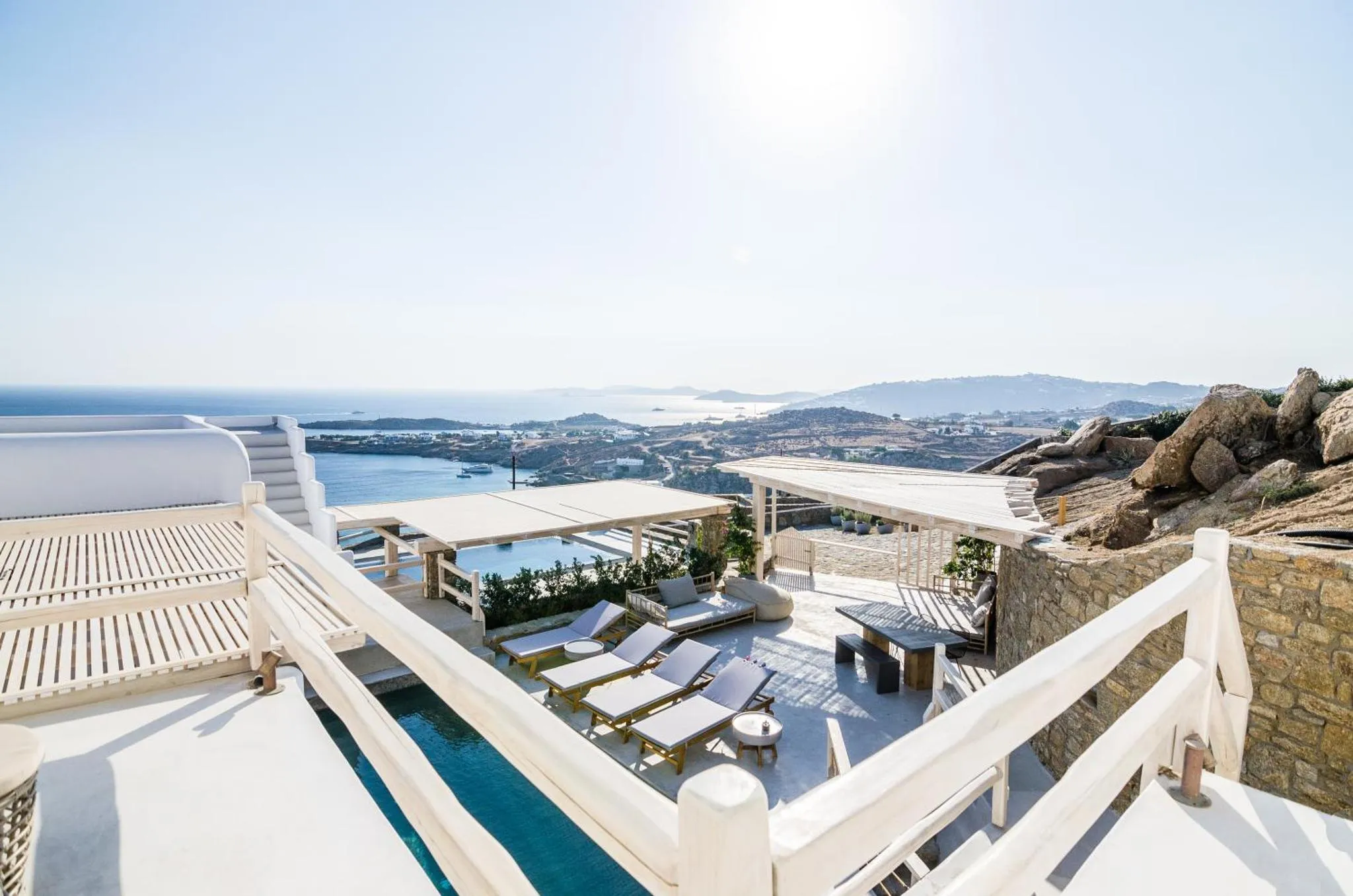 Terrasse avec transats et piscine offrant une vue sur la mer et le paysage environnant.