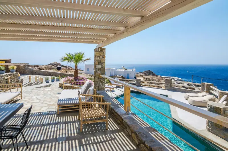 Terrasse ombragée avec mobilier d'extérieur donnant sur une piscine et la mer.