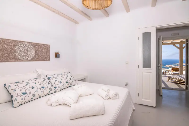 Une chambre lumineuse avec un lit décoré de coussins et une vue sur la mer.