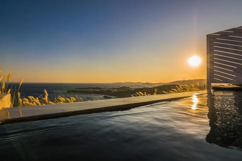 Une piscine à débordement reflète le soleil couchant sur la mer.