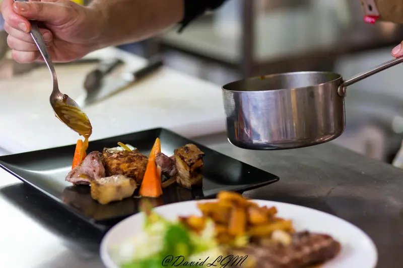 Un plat de viande est dressé avec soin par un chef en cuisine.