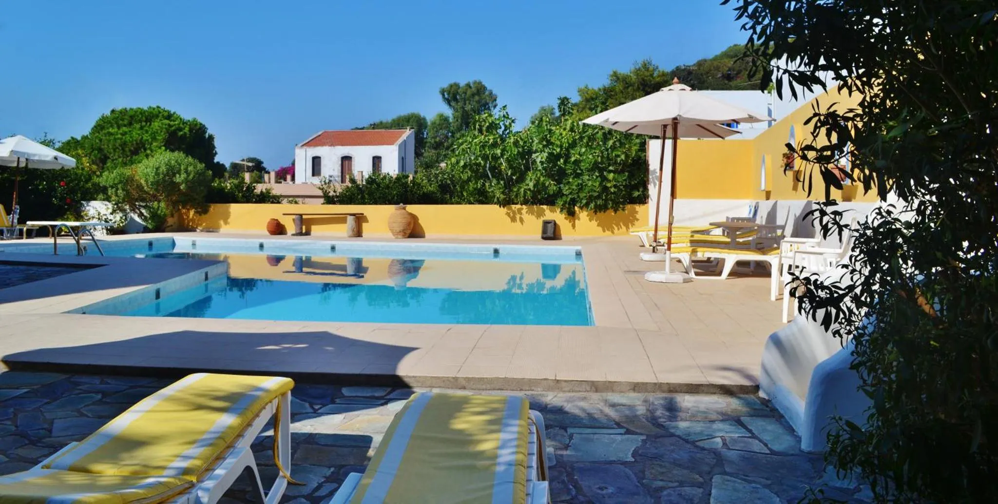 Transats blancs et parasols près d'une piscine ensoleillée.
