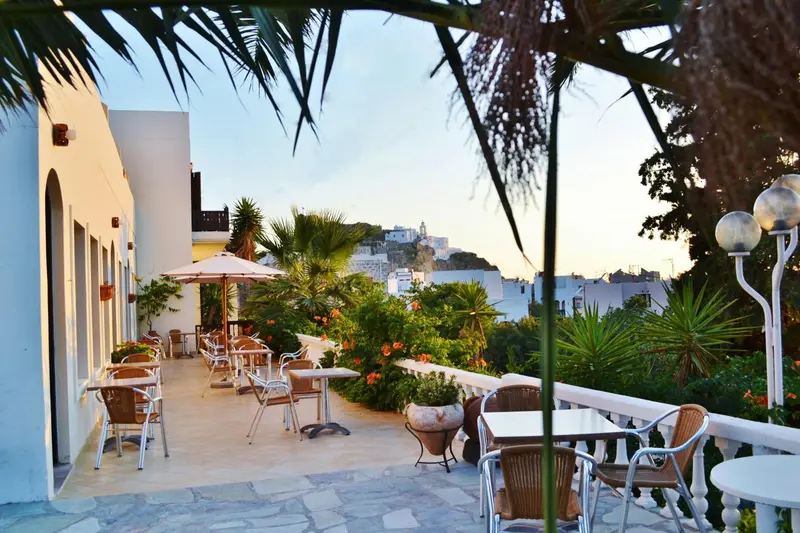 Terrasse ombragée avec tables et chaises donnant sur un paysage urbain.