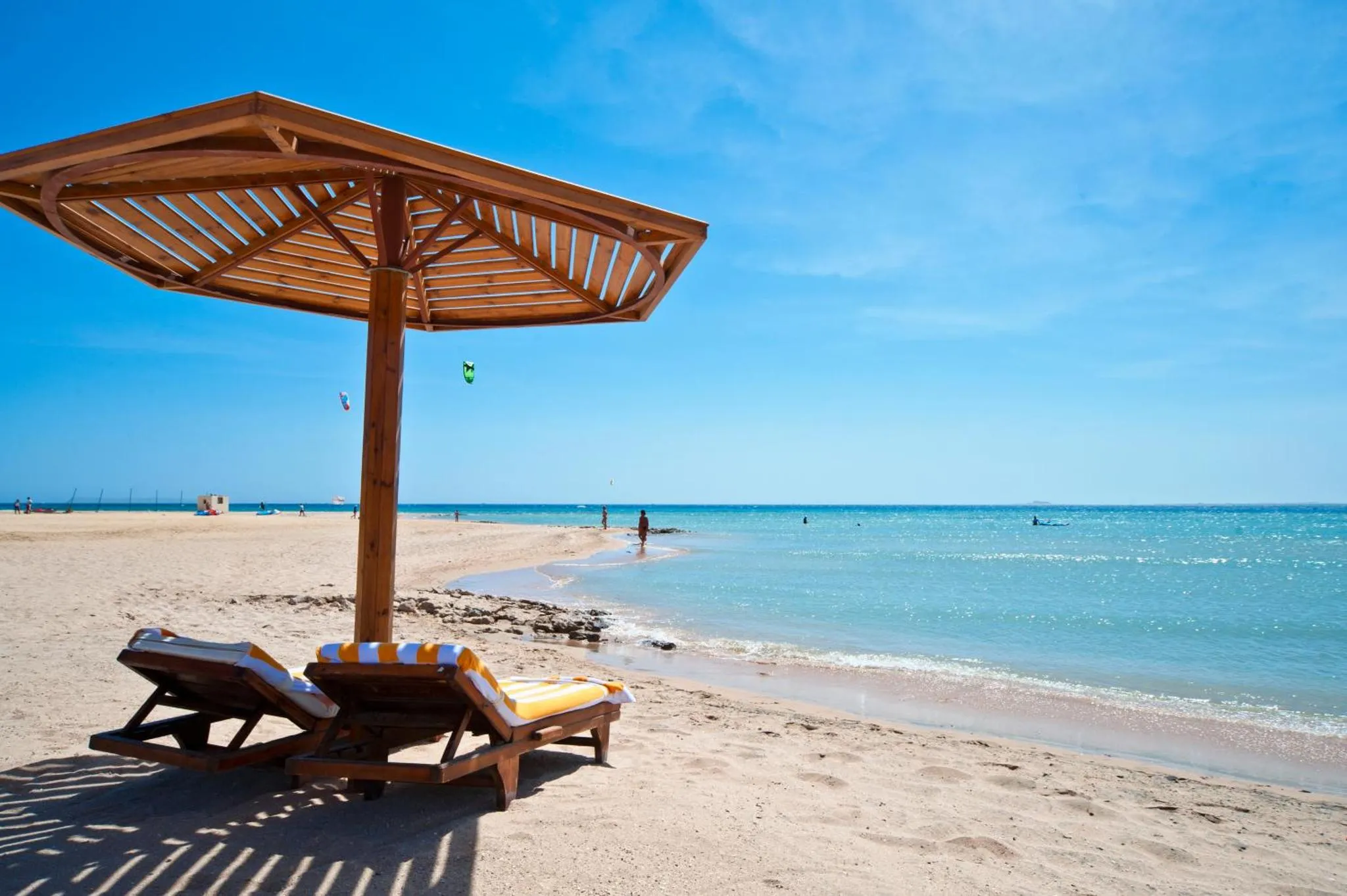 Deux transats à l'ombre d'un parasol sur une plage de sable fin.