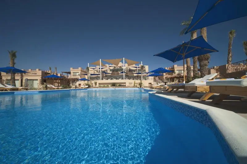 Piscine bleue bordée de transats sous un ciel bleu dégagé.