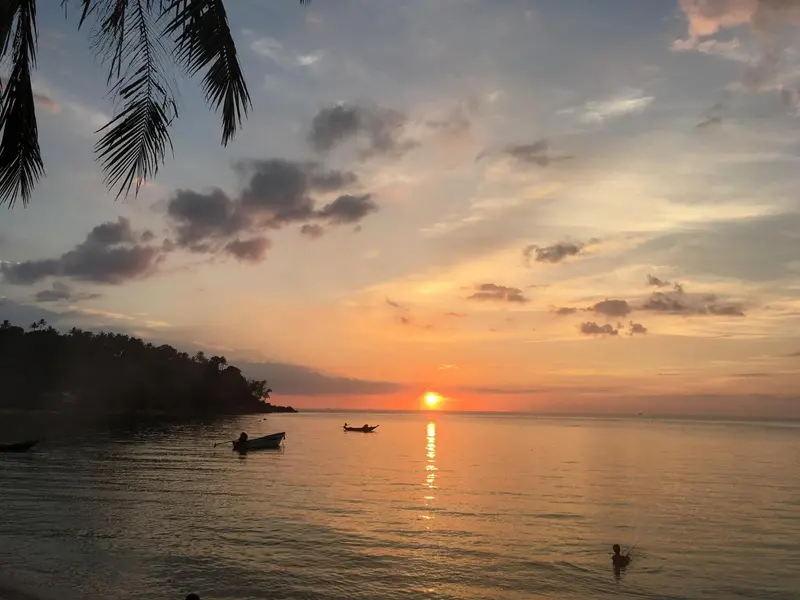 Coucher de soleil sur la mer avec quelques embarcations à l'horizon.