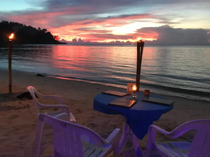 Table et chaises en plastique sur une plage au coucher du soleil.
