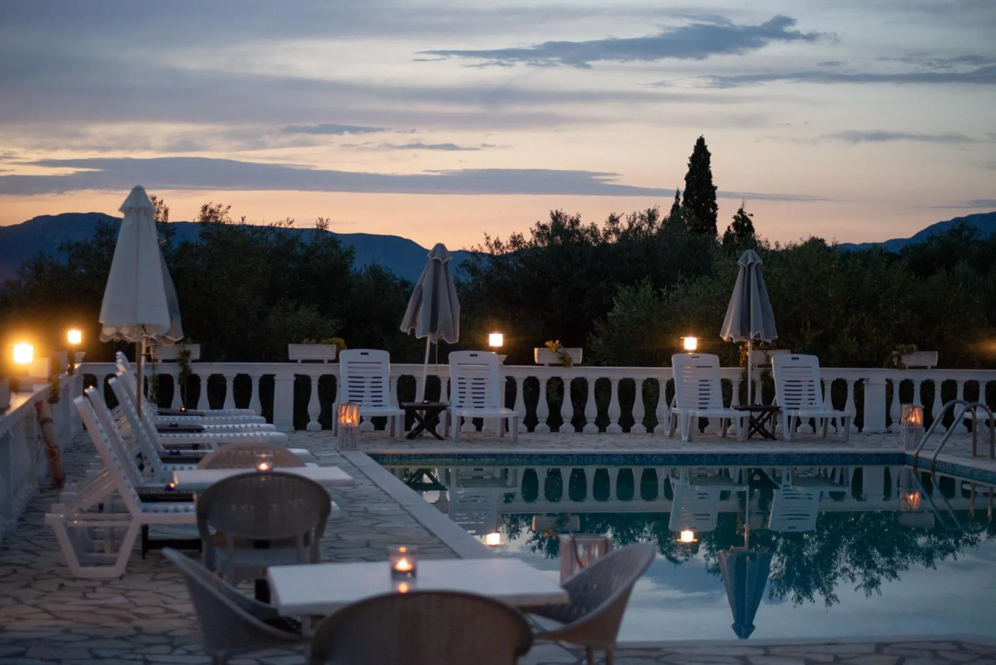 Terrasse avec transats et tables au bord d'une piscine illuminée au crépuscule.