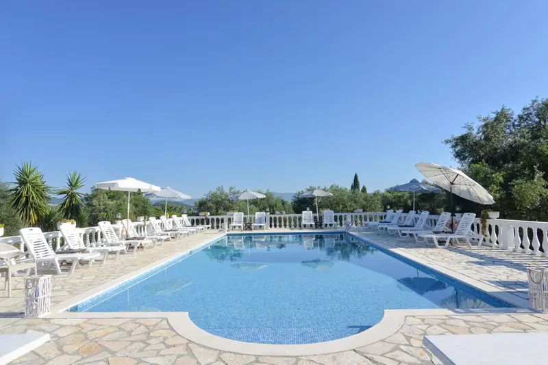 Transats blancs alignés au bord d'une piscine rectangulaire sous un ciel bleu dégagé.