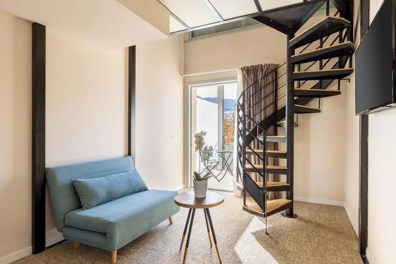 Un canapé bleu clair et un escalier en colimaçon noir dans une pièce lumineuse.
