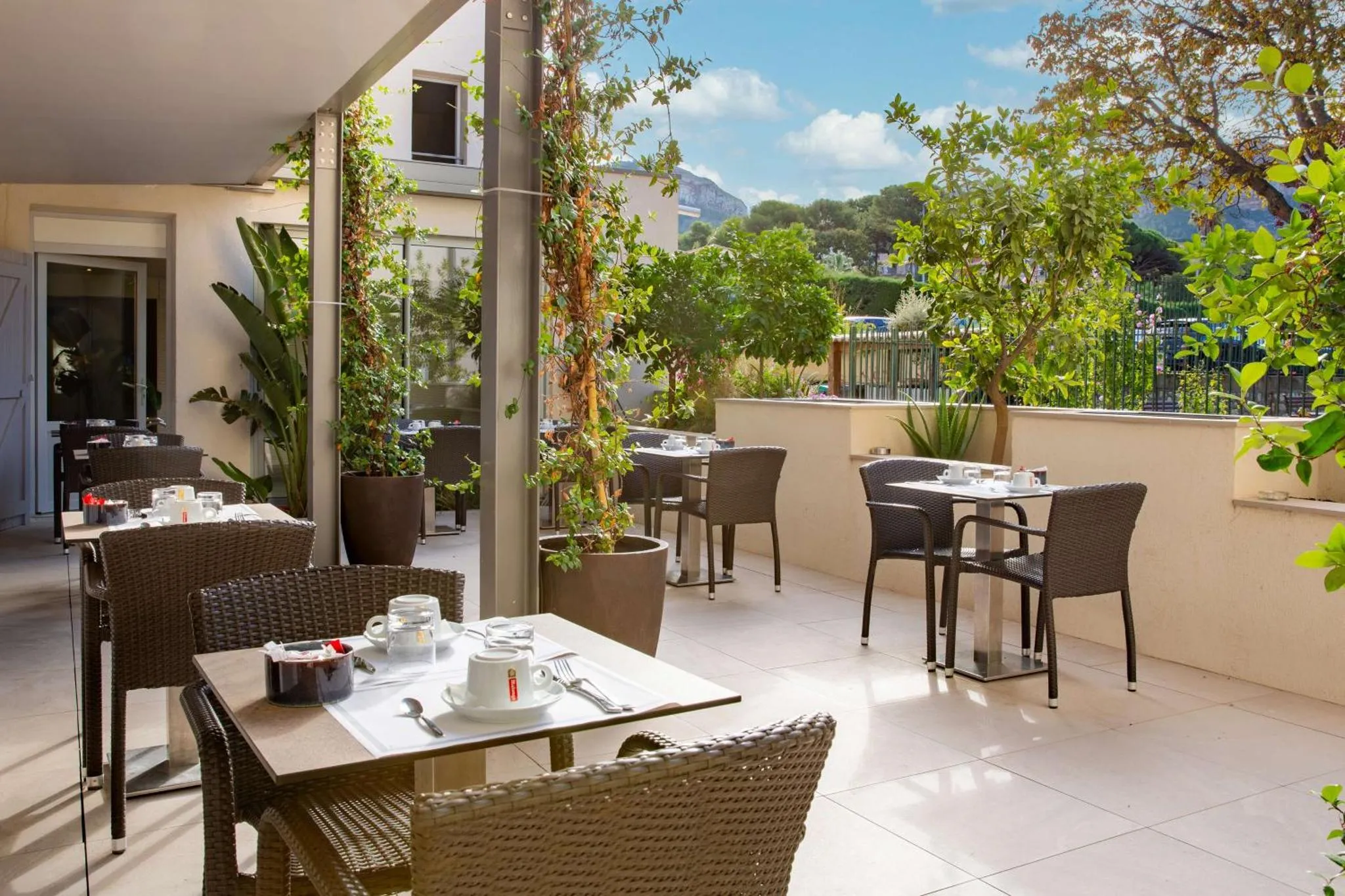 Tables et chaises disposées sur une terrasse ombragée avec vue sur la végétation.