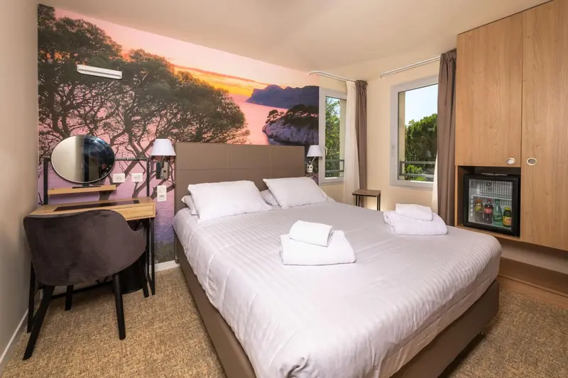 Chambre lumineuse avec un grand lit et un décor mural représentant un paysage.