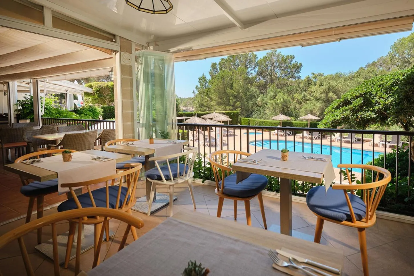 Tables dressées sur une terrasse ombragée avec vue sur une piscine et une végétation luxuriante.