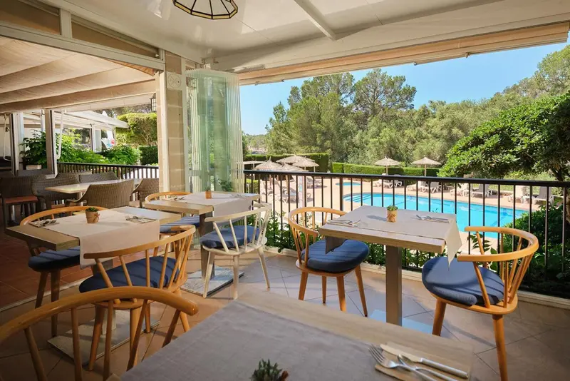 Tables dressées sur une terrasse ombragée avec vue sur une piscine et une végétation luxuriante.