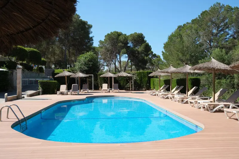 Une piscine rectangulaire bordée de transats sous des parasols en chaume.