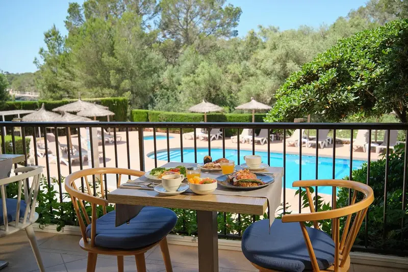 Une table de petit-déjeuner est dressée sur une terrasse avec vue sur une piscine.