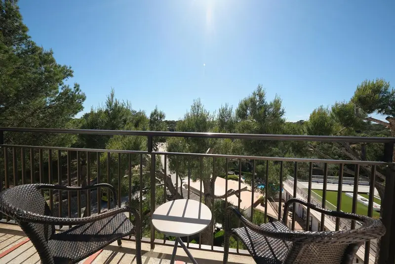 Terrasse avec mobilier en osier donnant sur une végétation luxuriante et une piscine.