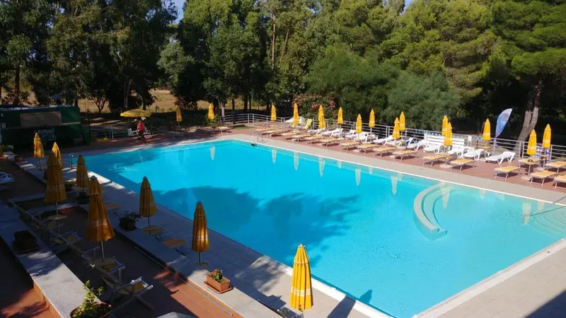 Une piscine rectangulaire entourée de transats sous des parasols.